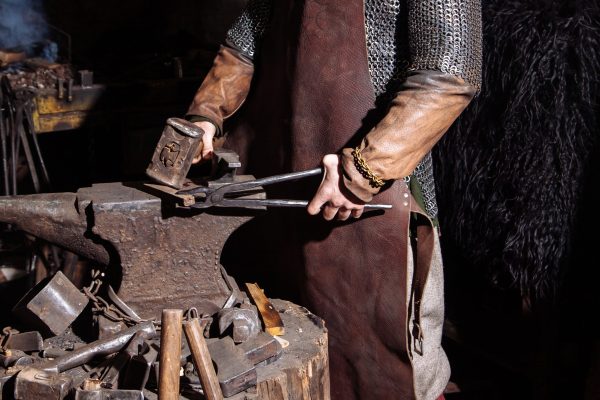 Viking forges weapons and swords in the smithy. A man in a warrior's clothes is in the smithy